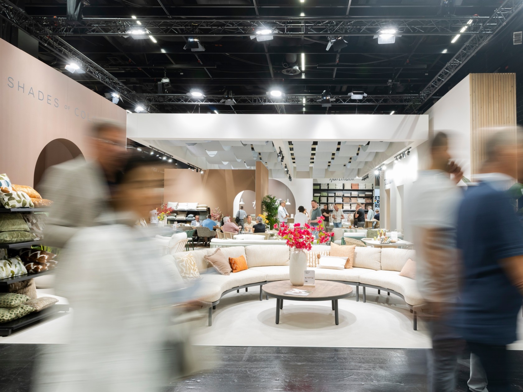 A lively trade show area featuring a curved couch, decorative flowers, and exhibits, with attendees moving through the space.