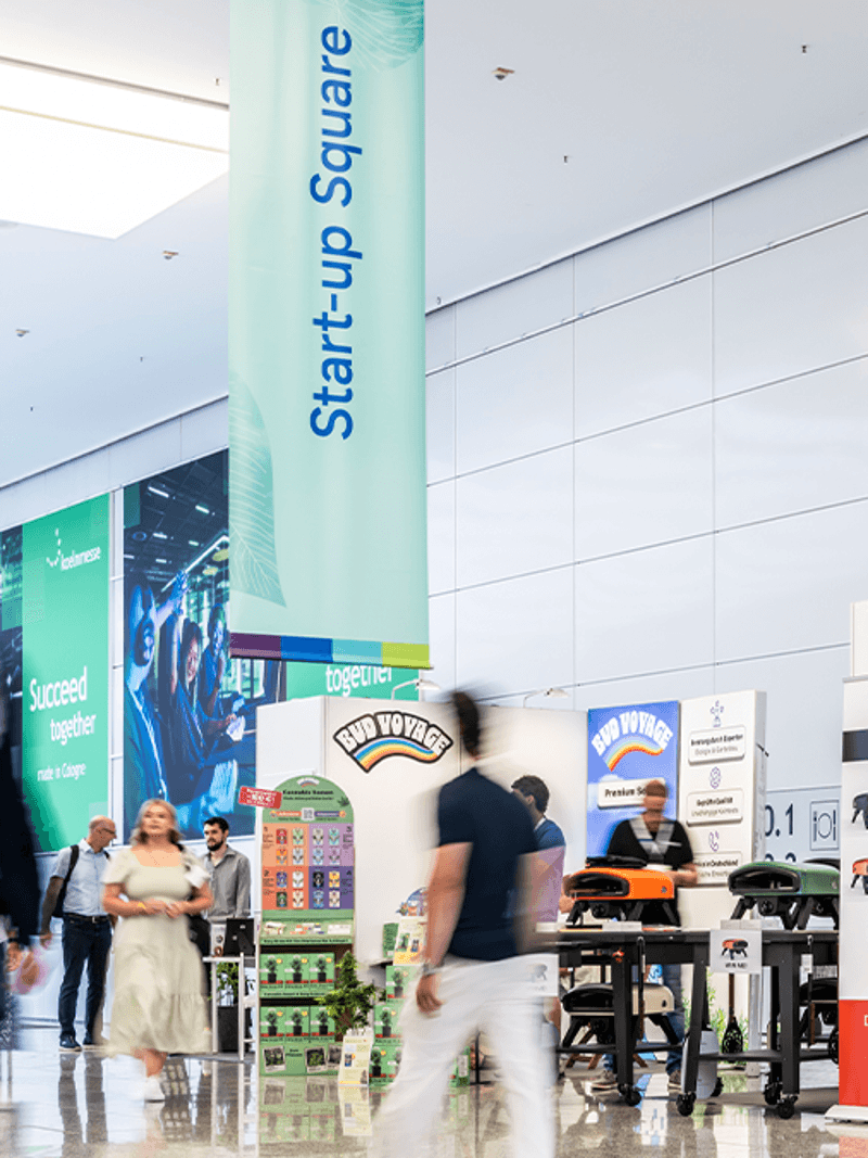 A bustling exhibition space with stands for "Smart Garden" and "nero," featuring banners and people walking by.