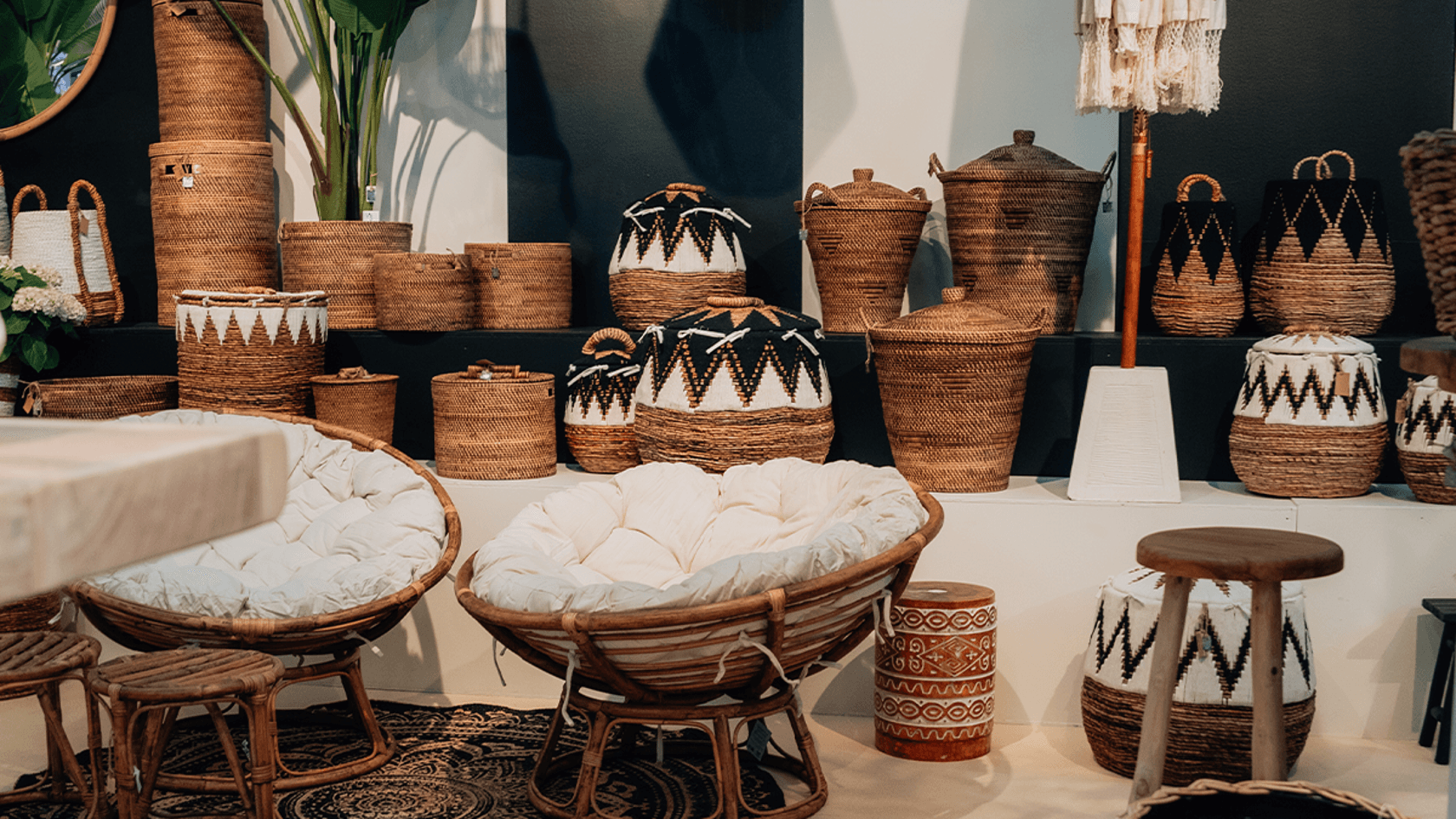 Impressionen Tag 2 spoga+gafa Eine Vielzahl von handgefertigten Weidenkörben in unterschiedlichen Formen und Größen wird harmonisch mit gemütlichen Rattanstühlen und einem Holzstuhl in einer stilvollen Präsentation vor einem dunklen Hintergrund zu einem einladenden Ambiente beim spoga+gafa Tag 2 kombiniert.