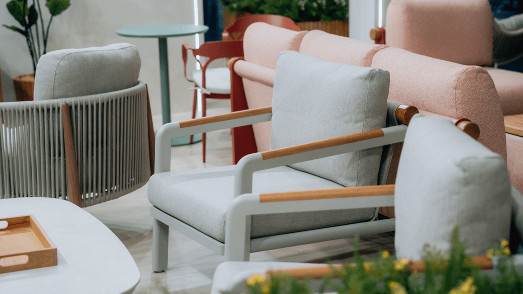 Impressionen Tag 2 spoga+gafa Ein stilvolles Wohnzimmer, das auf der spoga+gafa am zweiten Tag präsentiert wird, zeigt moderne graue und pinke Stühle, einen runden grünen Tisch und üppige Pflanzen im Hintergrund, die eine einladende Atmosphäre schaffen.
